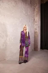 Camisa de corte recto y estructura clásica, con cuello camisero y cierre frontal de botones. Presenta un diseño estampado con motivos geométricos y florales en tonos violeta, marrón y verde.
