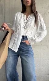 Camisa blanca de manga larga con detalles de encaje y diseño abotonado en la parte delantera.