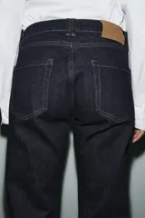 Jeans de tiro medio con corte slim leg, confeccionados en denim color beige. Presentan cintura con trabillas, diseño clásico de cinco bolsillos y cierre frontal con cremallera y botón metálico.