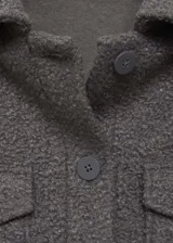 Chaqueta de tejido bouclé color gris oscuro, con diseño recto, cuello camisero, cierre frontal de botones y dos bolsillos de solapa con botón en el frente.