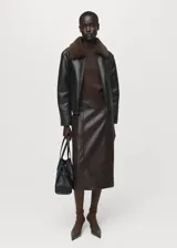 Chaqueta tipo coach de efecto piel en color negro, con diseño oversize, cierre frontal con cremallera, cuello camisero y forro interior de borreguito en color marrón.