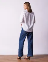 Camisa blanca de algodón con cuello clásico, escote en V y cierre frontal con botones. Presenta apliques de brillos plateados en el frente y mangas largas con puños abotonados.