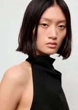 Top negro sin mangas de cuello halter drapeado, con bajo asimétrico y espalda abierta con tiras.