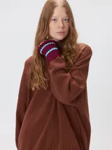 Pullover de punto color rojo, con cuello tortuga, corte holgado y mangas largas con puños acanalados en contraste con rayas blancas. Presenta un logo bordado en el pecho.