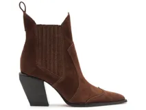 Bota texana de gamuza color marrón, con taco cuadrado negro y punta fina. Presenta paneles laterales elásticos con costuras verticales y una lengüeta en la parte superior trasera.