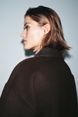 Chaqueta de corte recto confeccionada en hilatura con lana, en color marrón oscuro. Presenta cuello clásico en tejido efecto piel de ante, cierre frontal con cremallera metálica y manga larga.