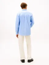 Camisa Tommy Hilfiger de corte regular en puro algodón Oxford, color celeste con sutiles rayas diplomáticas. Presenta cuello con botones, bolsillo de parche en el pecho con el logo bordado y mangas largas con puños redondeados.