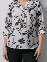 Blusa de gasa con estampado floral en tonos blanco y negro, cuello a la base con escote en V y cierre frontal parcial con botones. Presenta mangas tres cuartos con puños rectos.