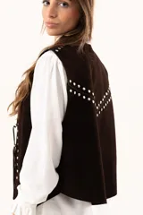 Chaleco oversize confeccionado en cuero descarne, con diseño de terminación en picos. Presenta lazos frontales con ojalillos metálicos y detalle de tachas metálicas en hombros y espalda.