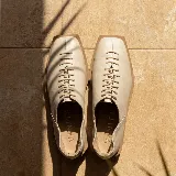 Zapato plano de cuero color beige, con diseño acordonado frontal, punta cuadrada y suela de goma.