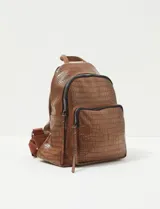 Mochila de cuero sintético con textura croco color marrón chocolate, con cierre principal y bolsillo frontal con cierre. Cuenta con tirantes ajustables y asa superior.