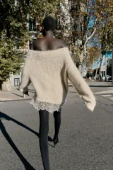 Jersey de punto con cuello barco y manga larga, confeccionado en tejido efecto cepillado. Presenta un diseño asimétrico en el bajo con detalle de encaje aplicado.