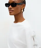 Remera de algodón color blanco, con cuello redondo, mangas cortas y detalle de lazos brillantes aplicados en las mangas.