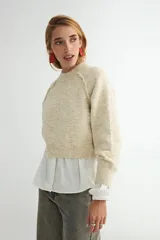 Buzo de tejido de punto con cuello redondo, diseño cropped y mangas largas con puños acanalados. Presenta una textura jaspeada en tono beige.