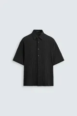 Camisa de corte regular fit con textura arrugada, cuello solapa y manga corta. Presenta cierre frontal con botones y aberturas laterales en el bajo.