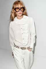 Camisa de manga larga con estampado de rayas verticales finas, cuello redondo con volante plisado y detalle de volante lateral en el frente. Cuenta con cierre frontal de botones y puños anchos.