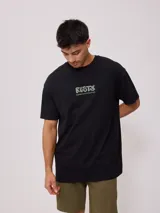 Remera negra de corte oversize, confeccionada en algodón. Presenta un estampado gráfico en el pecho con el logo de la marca y texto complementario.