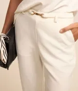 Pantalón capri blanco de crepé con trabillas en la cintura y cinturón fino con hebilla diferenciada.