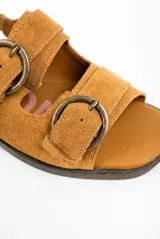 Sandalias planas de gamuza color tostado, con múltiples tiras decoradas con grandes hebillas metálicas en tono bronce viejo y tira ajustable en el talón.