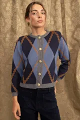 Cardigan de punto con patrón argyle en tonos azul marino, celeste y naranja. Presenta cuello redondo, cierre frontal con botones dorados y terminaciones en tejido acanalado gris.