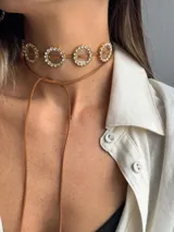 Choker de cuero sintético color marrón claro con cuatro dijes redondos dorados, cada uno con incrustaciones de strass y una resina transparente en el centro.