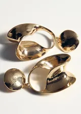 Aros colgantes dorados de diseño geométrico y orgánico, formados por un disco superior texturizado y una pieza inferior de forma ovalada e irregular con efecto drapeado.