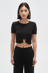 Top de manga corta color negro con textura arrugada, cuello redondo y detalle de frunce frontal con argolla metálica y botones decorativos.