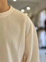 Buzo oversize de tejido waffle en color beige, con cuello redondo y manga larga, con pequeña etiqueta de marca en el dobladillo inferior.