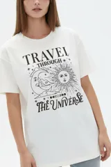 Remera de algodón manga corta, corte holgado, con cuello redondo y estampado frontal en negro con la frase "Travel through the universe" y motivos celestes de sol, luna y estrellas.