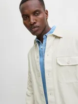 Sobrecamisa de manga larga confeccionada en sarga de algodón, con cuello camisero, cierre frontal de botones y un bolsillo en el pecho. Presenta un corte amplio y estructura versátil ideal para usar como capa ligera.