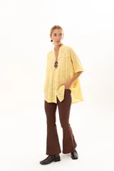 Camisa de corte oversize confeccionada en tela bordada con diseño calado, color amarillo. Presenta cuello mao, cierre frontal con botones y mangas cortas amplias.