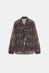 Blusa semitransparente con estampado paisley en tonos rosa, verde y beige sobre fondo negro. Presenta cuello redondo con escote en pico y lazada con borlas doradas. Tiene manga larga y cierre frontal con botones. Incluye forro interior.