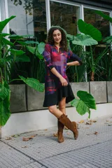 Vestido corto con estampado geométrico en tonos violeta, rojo y negro, confeccionado en jersey elastizado con efecto gamuzado. Presenta cuello redondo y mangas 3/4 con puños abotonados. La falda es de corte irregular con volados.