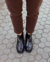 Botinetas de cuero negro con paneles laterales de gamuza al tono. Presentan una suela track robusta con taco cuadrado y cierre lateral para facilitar el calce.