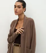 Cardigan de punto color marrón, de corte largo y holgado, con cuello tipo chal, mangas largas y bolsillos delanteros funcionales.