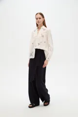 Camisa de algodón blanca de corte holgado, con cuello camisero, mangas largas y bordados florales multicolores. Presenta detalles de calados en los hombros y cierre frontal con botones.
