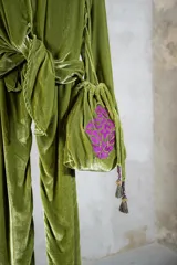 Cartera tipo saco de terciopelo de seda color verde oliva, con cierre de cordón ajustable y terminaciones de borlas con flecos. Presenta un bordado decorativo en color fucsia en el frente.