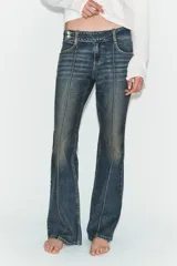 Jeans de tiro bajo con corte bootcut, confeccionados en denim con efecto lavado. Presentan costuras verticales marcadas en el frente, cierre frontal con cremallera, gancho metálico y detalle de trabilla con botones en la cintura.