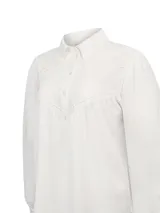 Blusa de algodón orgánico color blanco, con cuello camisero, cierre frontal parcial con botones y mangas largas. Presenta detalles de bordado inglés en el pecho y en los puños.