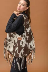 Bolso tipo hobo de gran capacidad con estampado animal print de vaca en tonos marrón y blanco. Presenta una etiqueta de cuero con el logo de la marca en el frente y un diseño de caída relajada.