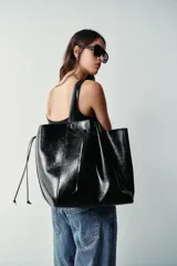Bolso tipo shopper color negro, con diseño fruncido en la parte delantera y doble asa de hombro.