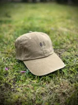 Gorra tipo dad hat en color gris lavado, con diseño de dos hojas bordadas en hilo negro en la parte frontal. Cuenta con visera curva y estructura flexible.