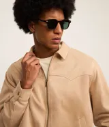 Campera masculina de estilo casual con cuello inglés, cierre frontal por cremallera, bolsillos laterales y ajuste elástico en el bajo. Presenta detalles de recortes en la parte superior delantera.