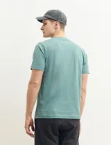 Remera color petróleo de manga corta con estampa de un edificio y texto en el frente.