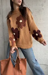 Sweater de punto grueso color camel, con diseño de flores grandes aplicadas en tonos marrones y centro crema. Presenta cuello redondo alto, mangas largas con hombros caídos y terminaciones acanaladas.