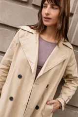 Trench clásico de largo midi en color beige, con diseño de doble abotonadura, solapas amplias, detalles en hombros y correas ajustables en los puños.