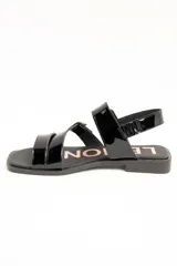 Sandalias planas de cuero negro charol con doble tira frontal ajustable mediante hebillas metálicas y tira en el talón.