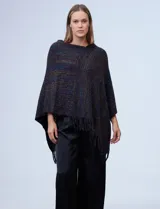 Poncho tejido en hilo soft, con efecto jaspeado multicolor (predominantemente tonos oscuros como azul marino, negro, y toques de violeta y dorado/lurex). Presenta un diseño asimétrico y flecos largos en los bordes.