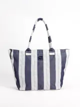 Bolso tipo tote grande, resistente al agua, con diseño de rayas verticales rojas y blancas. Cuenta con asas largas de hombro, cierre superior y parche de cuero con logo grabado. Incluye neceser transparente a juego con base y detalles a rayas.