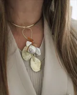 Gargantilla rígida dorada con colgante de piedras irregulares color blanco, naranja y dorado, y dijes de metal dorado en forma de hojas.